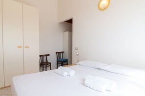 A hotel room with a bed, two chairs, a wardrobe, and a mirror.
