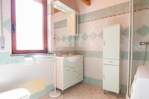 A bathroom with a toilet, sink, mirror, cabinet, and shower.