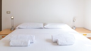 Una habitación de hotel limpia y minimalista, con una cama bien hecha, dos lámparas de noche y una mesita de madera.