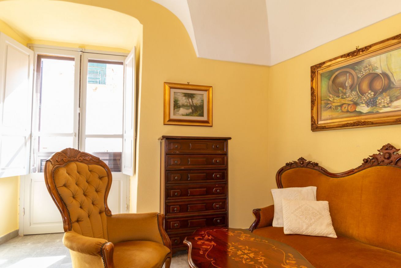 Une pièce avec une grande fenêtre, une chaise en bois, un canapé, un meuble en bois et un tableau accroché au mur.