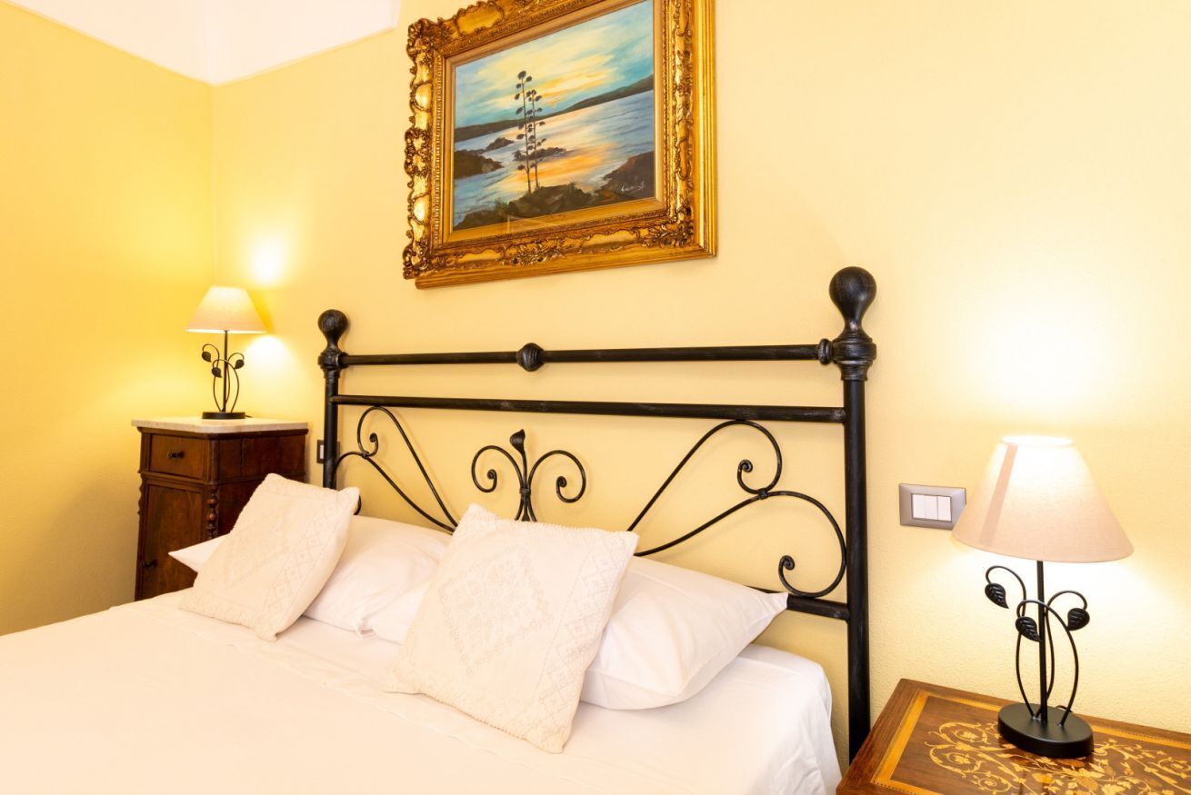 A bed with white linens, a painting above it, and two bedside lamps.