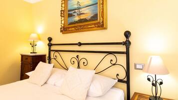 A bed with white linens, a painting above it, and two bedside lamps.