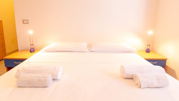 A hotel room with a bed, two bedside lamps, and two rolled towels. - Residenza Le Vigne-ground floor (Cuglieri)