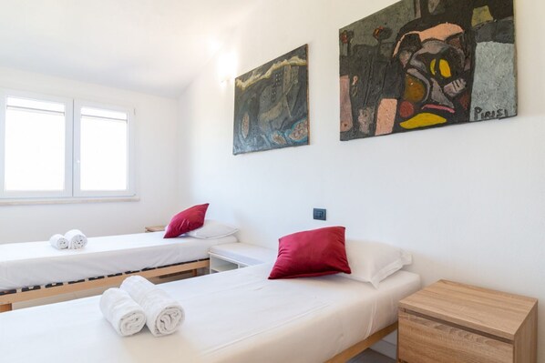 Een hotelkamer met twee bedden, een houten nachtkastje, een kleine tafel en twee schilderijen aan de muur.