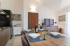A modern kitchen with a dining table set for four, a television, and a door with a light above it. - Casa D'Autore | Cabras with parking (Cabras)