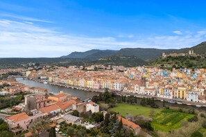 A coastal cityscape with a river, historic buildings, and a hilltop fortress. - Bosa Eye House 1873 | Castle (Bosa)
