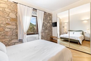 A bedroom with a stone wall, a bed, a TV, and a large mirror. - Bosa Eye House 1873 | Castle (Bosa)