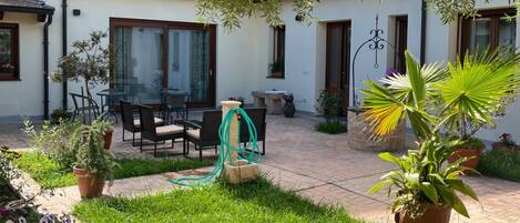 A patio with outdoor furniture, a garden, and a building with windows and doors.