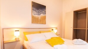 A neatly made bed with white and yellow pillows, a bedside lamp, and a folded towel on the side. -  Domo Mea Rooms- Camera 4 (CABRAS)