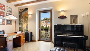 Een kamer met een piano, een bureau, een bankje en uitzicht op een stad door een deur.