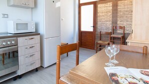 Een keuken met een magnetron, oven en koelkast. Er staat een eettafel met stoelen en een tijdschrift.