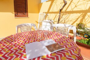 A table with a patterned tablecloth, two white chairs, and a menu on the table.