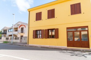A yellow building with brown shutters, a balcony, and a large window.