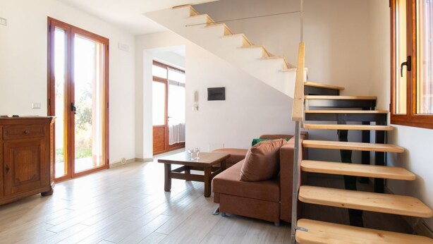 Een trap met houten treden die leidt naar een verdieping, een bruine bank, een houten tafel en een houten kast.