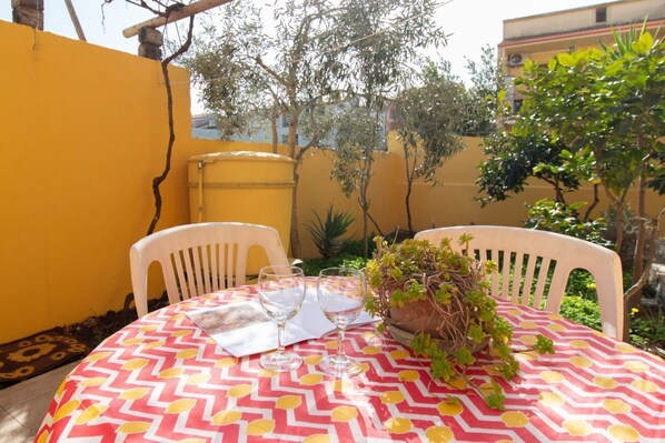 A round table with a patterned tablecloth, two white chairs, and a potted plant with green foliage.