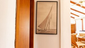 A framed black and white photograph of a sailboat on the water, a wooden door, and a dining area with wicker furniture. - S'Imbucada Home-Mare e Relax (SAN VERO MILIS)