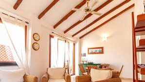 A room with wicker furniture, a ceiling fan, wooden beams, a dining area, and wall clocks. - S'Imbucada Home-Mare e Relax (SAN VERO MILIS)