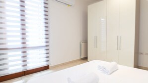 Une chambre d’hôtel avec un lit, deux serviettes enroulées, un radiateur et une fenêtre avec des stores.