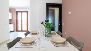 Un coin repas avec une table dressée pour quatre personnes, des chaises, un vase avec des plantes et une porte en arrière-plan.