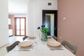 Comedor con una mesa preparada para cuatro personas, sillas, un florero con plantas y una puerta al fondo.