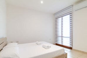 Un dormitorio limpio y moderno con una cama individual, ropa de cama blanca y una ventana con persianas.