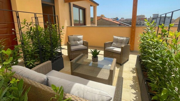 Un balcon agrémenté de meubles en osier, d’une table en verre et de plantes en pot.
