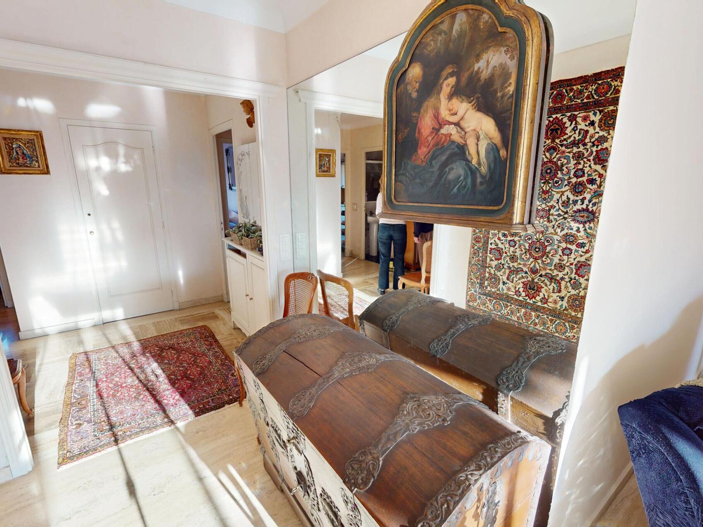 A room with a large bed, a painting, a patterned rug, and a white door.