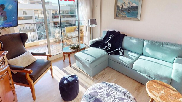 A living room with a sofa, armchair, and ottoman, a glass table, and a painting on the wall. - Pleasant 3P in Menton with terrace and garage (Menton)