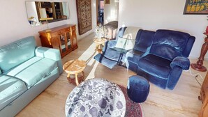 A living room with a light blue sofa, a dark blue sofa, a patterned ottoman, a wooden cabinet, and a mirror on the wall. - Pleasant 3P in Menton with terrace and garage (Menton)