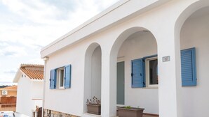Un bâtiment blanc avec des volets bleus, portant le numéro 20, et un balcon orné de plantes en pot.