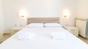 Une chambre d’hôtel comprenant un lit, deux tables de chevet, une petite table, un radiateur et des lampes fixées au mur.