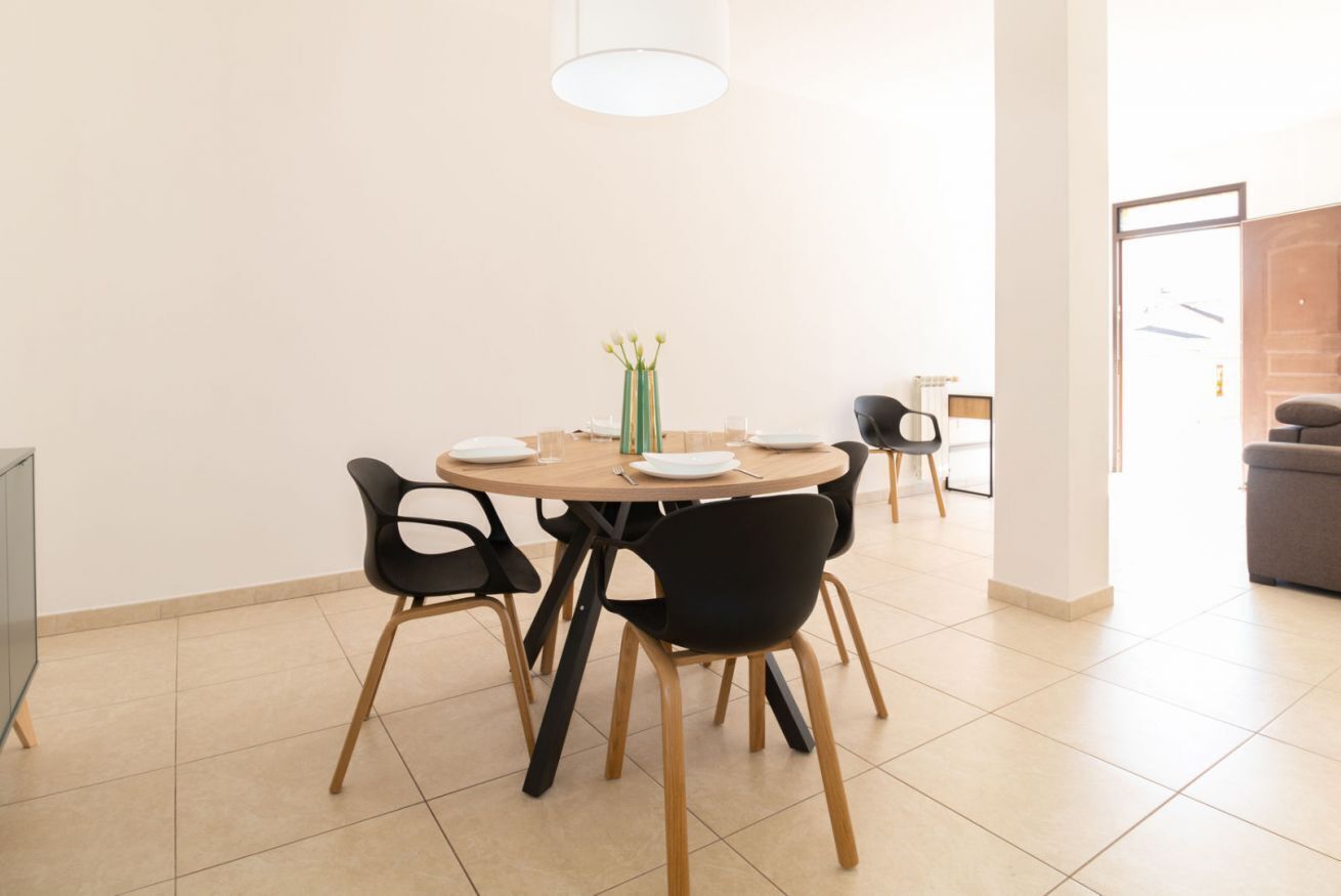 Un coin repas avec une table ronde, des chaises noires, un vase de fleurs et un luminaire suspendu.