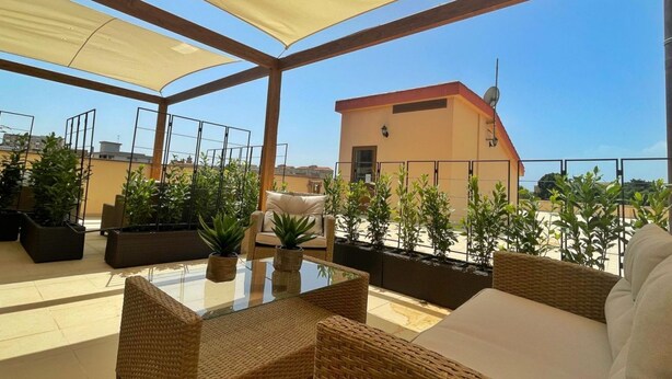 Une terrasse sur le toit, aménagée avec des meubles en osier, des plantes en pot et offrant une vue dégagée sur le paysage urbain.