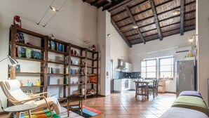 A spacious living area with a high ceiling, a wooden bookshelf, a dining table, and a kitchen in the background. - In Barberia- Cozy Corner (Milis)