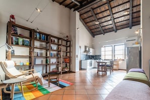A spacious living area with a high ceiling, a wooden bookshelf, a dining table, and a kitchen in the background. - In Barberia- Cozy Corner (Milis)