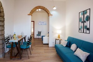 A dining area with a table and chairs, a sofa, a lamp, and a painting on the wall. - Josto Panoramic- Sea view (Cuglieri)
