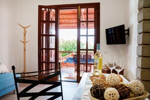 A room with a wooden door, a television mounted on the wall, a table with a bottle and glasses, and a blue sofa. - Josto Panoramic- Sea view (Cuglieri)
