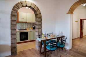 Un comedor con una mesa dispuesta para cuatro, una cocina visible a través de un arco y un suelo de madera.