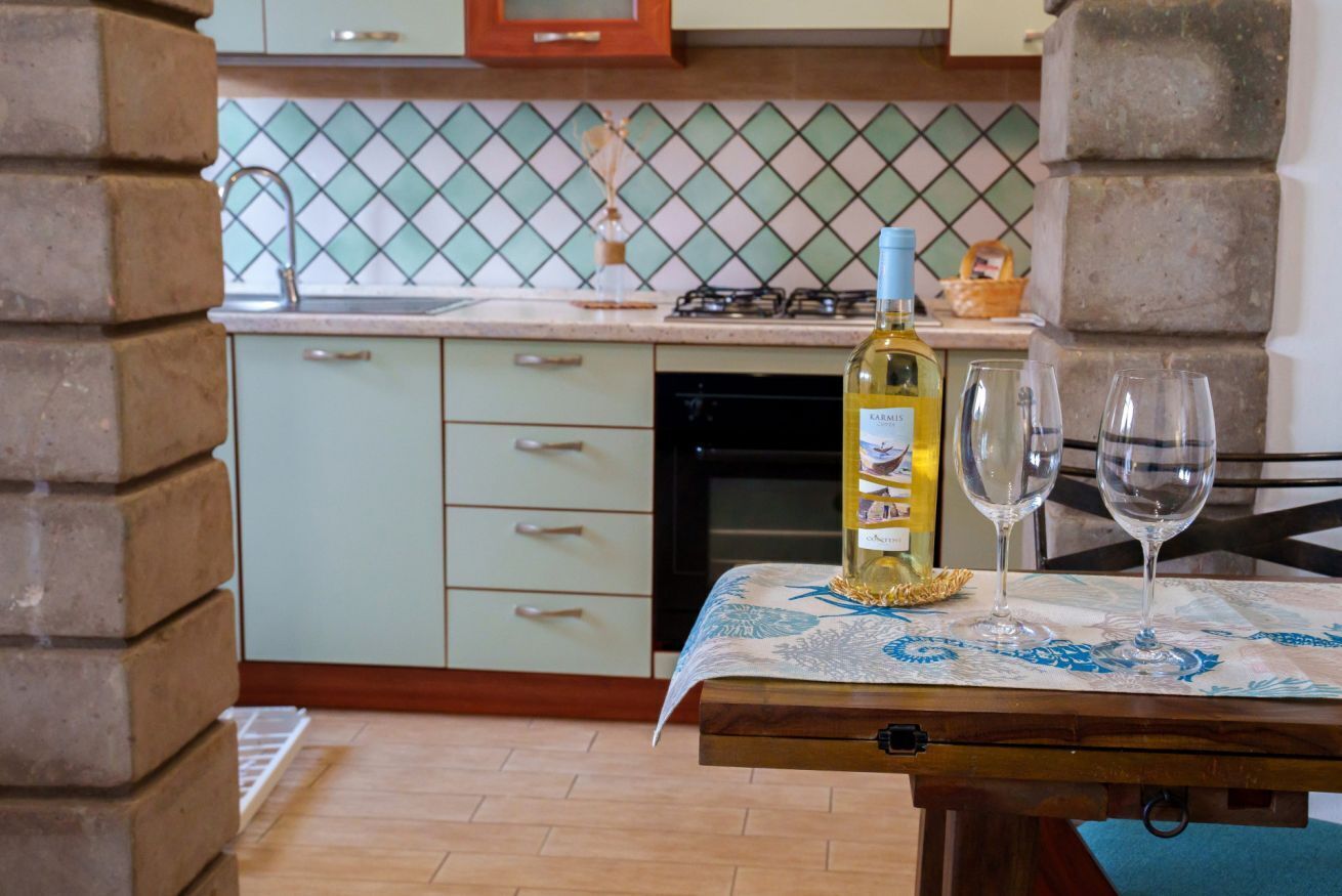 A kitchen with a tiled backsplash, a bottle of wine, and two glasses on a table.
