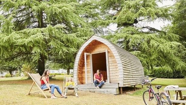Une petite cabane en bois, dotée d’un toit à deux versants, située sur une pelouse, avec des arbres en arrière-plan.