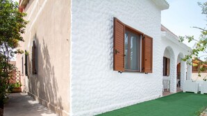 Um edifício branco com persianas de madeira, um gramado sintético verde e um caminho que leva a uma porta.