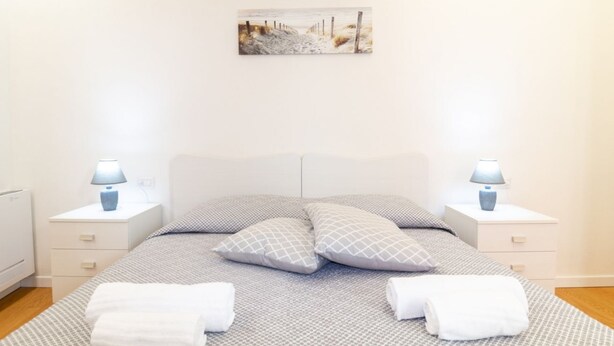 A neatly made bed with a patterned bedspread, two bedside lamps, and a painting on the wall. - Casa Sofia-Modern Apartment (Oristano)
