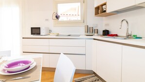 A modern kitchen with white cabinets, a microwave, a sink, and a window above the countertop. - Casa Sofia-Modern Apartment (Oristano)