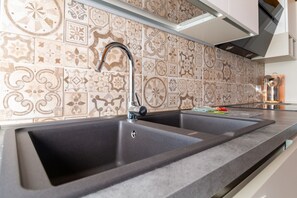 A kitchen with a double sink, patterned backsplash, and modern cabinetry. - Casa degli Artigiani (Oristano)