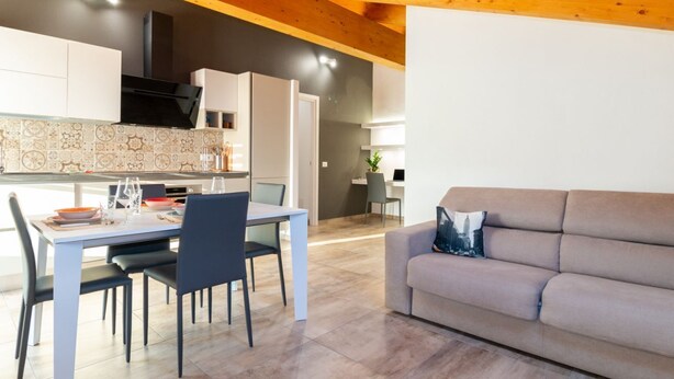 Une cuisine moderne avec des meubles blancs, une table à manger avec des chaises et un canapé gris dans l’espace salon.