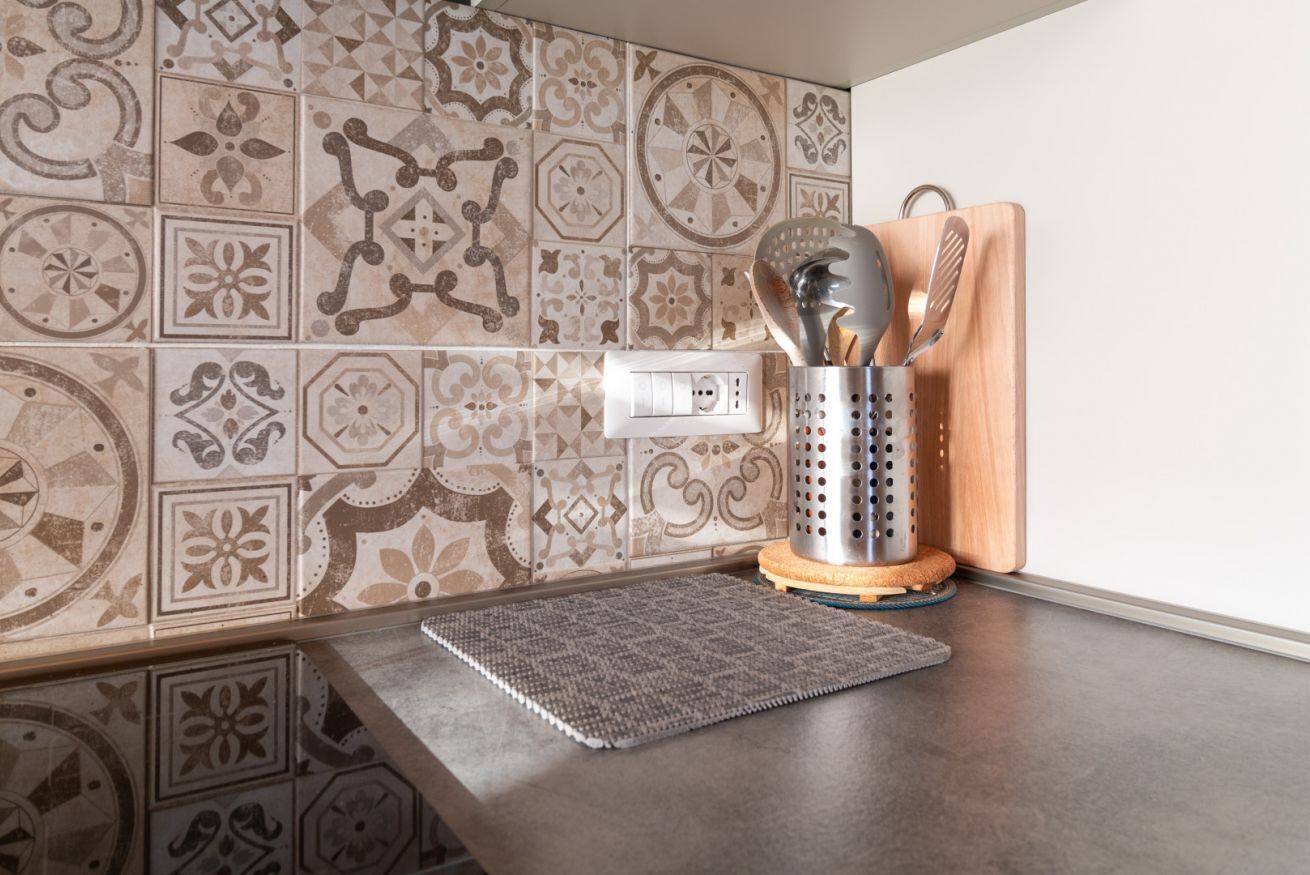 A kitchen with patterned tiles, a cutting board, a grater, and a notepad on the counter.