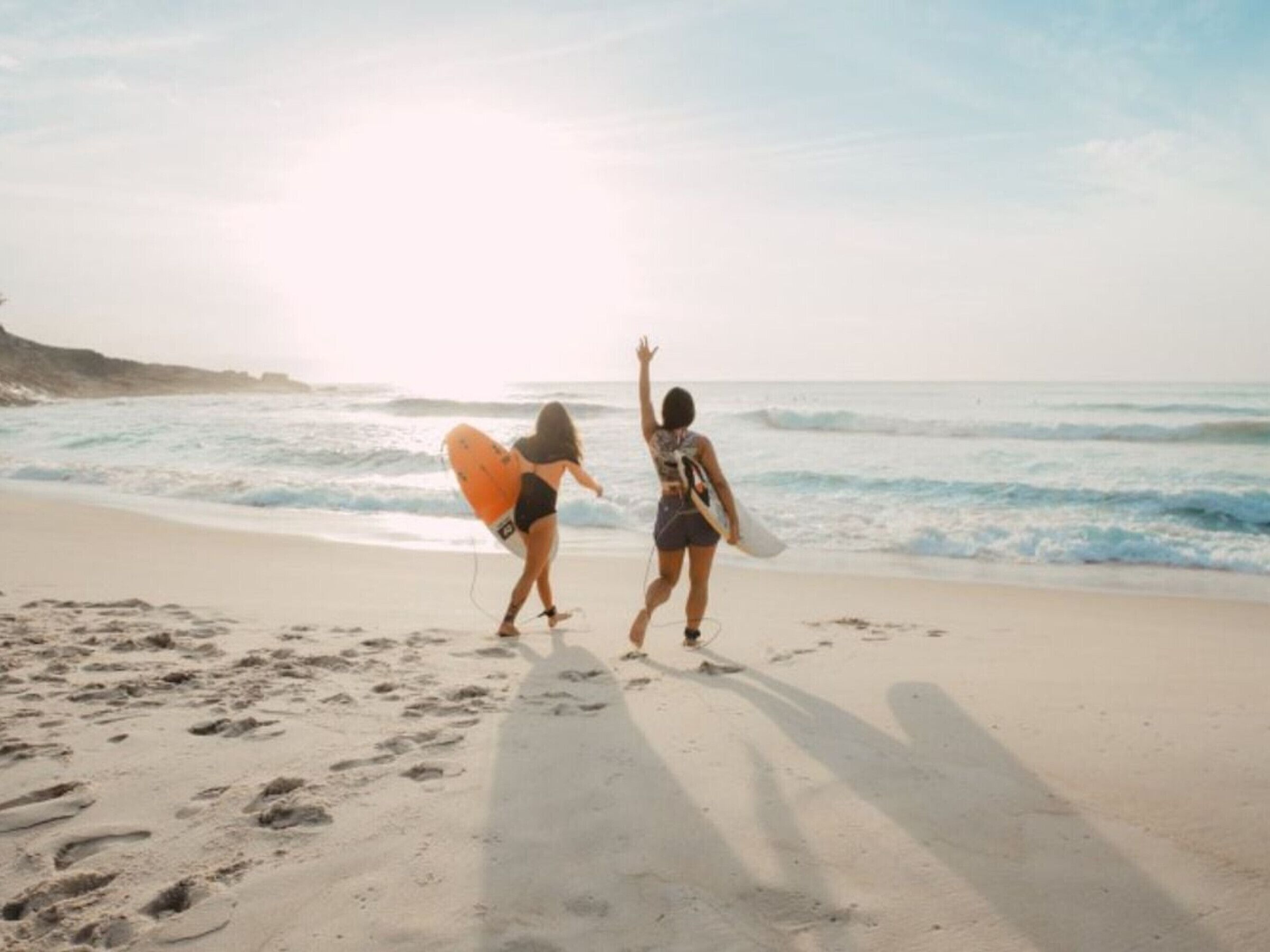 Two people walking on a sandy beach with ocean waves in the background.