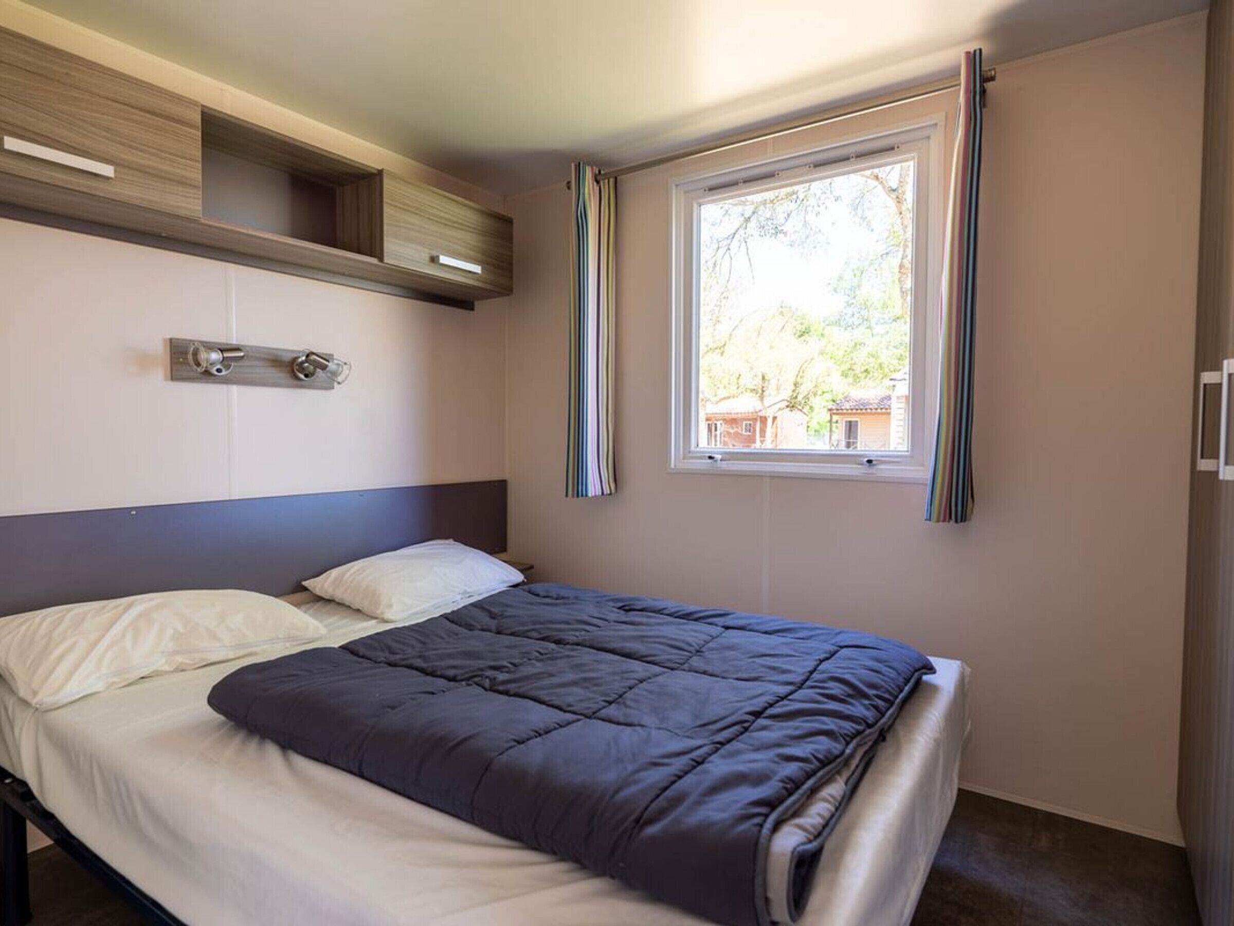 A bedroom with a bed, a window with curtains, a bedside table, and built-in shelving.