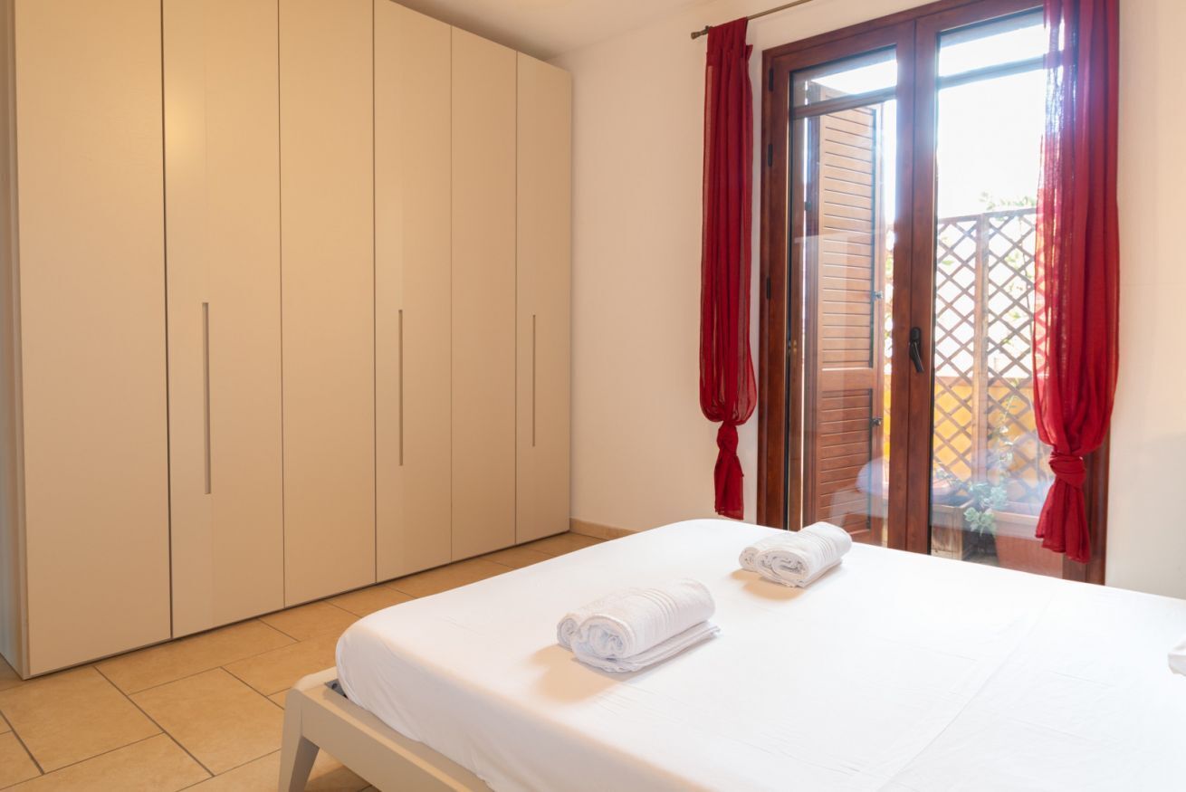 A bedroom with a bed, white curtains, and a sliding glass door to the outside.