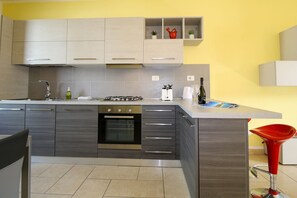 Une cuisine moderne avec des meubles gris, un four encastré, une cuisinière à gaz et un tabouret de bar rouge.
